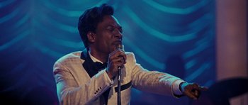 Movie still from “Dreamgirls” (2006), directed by Bill Condon – A man in a white jacket is singing into a microphone; Close Up shot, High angle