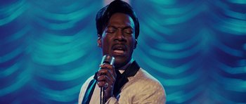 Movie still from “Dreamgirls” (2006), directed by Bill Condon – A man in a white jacket is singing into a microphone; Close Up shot, Over the shoulder angle