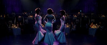 Movie still from “Dreamgirls” (2006), directed by Bill Condon – A group of three women standing next to each other on a stage; Wide shot, Over the shoulder angle