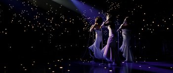 Movie still from “Dreamgirls” (2006), directed by Bill Condon – A group of women singing on a stage with lights in the background; Wide shot, High angle
