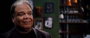 Movie still from “Dreamgirls” (2006), directed by Bill Condon – An older man in a black shirt is smiling for the camera; Close Up shot, Over the shoulder angle