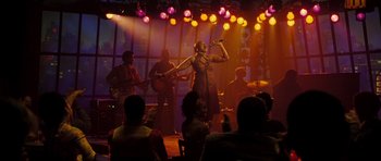 Movie still from “Dreamgirls” (2006), directed by Bill Condon – A group of people on a stage with a woman singing into a microphone; Wide shot, High angle