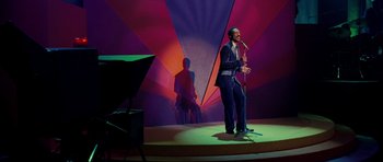 Movie still from “Dreamgirls” (2006), directed by Bill Condon – A man standing on a stage holding a microphone; Wide shot, High angle