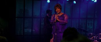 Movie still from “Dreamgirls” (2006), directed by Bill Condon – A woman in a purple dress singing into a microphone; Medium shot, Over the shoulder angle