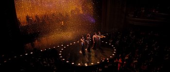 Movie still from “Dreamgirls” (2006), directed by Bill Condon – A group of people standing on a stage in front of lights; Extreme Wide shot, High angle
