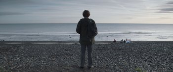 Movie still from “Frank” (2014), directed by Lenny Abrahamson – A man standing on the beach looking out at the ocean; Wide shot, Over the shoulder angle