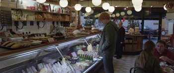 Movie still from “Frank” (2014), directed by Lenny Abrahamson – A man standing in front of a display case of food; Wide shot, Over the shoulder angle