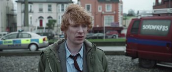 Movie still from “Frank” (2014), directed by Lenny Abrahamson – A young man with red hair and a tie; Close Up shot, Over the shoulder angle