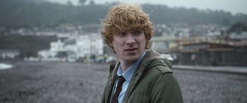 Movie still from “Frank” (2014), directed by Lenny Abrahamson – A young man with red curly hair wearing a jacket and tie; Close Up shot, Over the shoulder angle