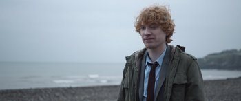 Movie still from “Frank” (2014), directed by Lenny Abrahamson – A man with red curly hair standing on the beach; Close Up shot, Over the shoulder angle