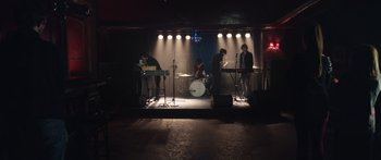 Movie still from “Frank” (2014), directed by Lenny Abrahamson – A group of people playing musical instruments on a stage; Wide shot, High angle