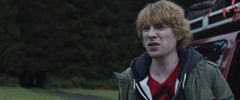 Movie still from “Frank” (2014), directed by Lenny Abrahamson – A man with red hair and a red shirt is standing in front of trees; Close Up shot, Over the shoulder angle