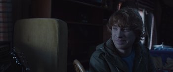 Movie still from “Frank” (2014), directed by Lenny Abrahamson – A man sitting in front of a chair in a room; Close Up shot, Over the shoulder angle