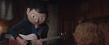 Movie still from “Frank” (2014), directed by Lenny Abrahamson – A person with a mask on playing a guitar; Medium shot, Over the shoulder angle