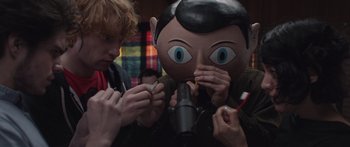 Movie still from “Frank” (2014), directed by Lenny Abrahamson – Two people are holding a cigarette in their hands; Medium shot, Over the shoulder angle