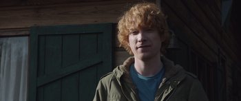 Movie still from “Frank” (2014), directed by Lenny Abrahamson – A young man with red curly hair wearing a green jacket; Close Up shot, Over the shoulder angle