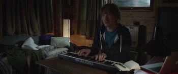 Movie still from “Frank” (2014), directed by Lenny Abrahamson – A young man is playing an electronic keyboard; Medium shot, Over the shoulder angle