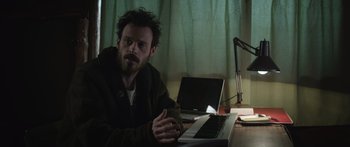 Movie still from “Frank” (2014), directed by Lenny Abrahamson – A man sitting in front of a laptop computer on top of a desk; Medium shot, High angle