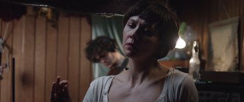 Movie still from “Frank” (2014), directed by Lenny Abrahamson – A woman with her eyes closed looking at a man in the background; Close Up shot, Over the shoulder angle