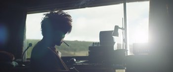 Movie still from “Frank” (2014), directed by Lenny Abrahamson – A man smoking a cigarette in front of an open window; Medium shot, Over the shoulder angle