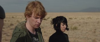 Movie still from “Frank” (2014), directed by Lenny Abrahamson – A man and a woman standing next to each other in the desert; Medium shot, Over the shoulder angle