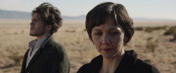 Movie still from “Frank” (2014), directed by Lenny Abrahamson – A woman standing next to a man on a dirt field; Close Up shot, Over the shoulder angle