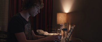 Movie still from “Frank” (2014), directed by Lenny Abrahamson – A man sitting in front of a laptop computer; Medium shot, Low angle