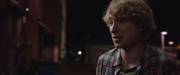 Movie still from “Frank” (2014), directed by Lenny Abrahamson – A man with a beard and a checkered shirt is smiling; Close Up shot, Over the shoulder angle