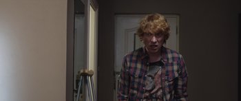 Movie still from “Frank” (2014), directed by Lenny Abrahamson – A young man standing in front of a mirror in a room; Medium shot, Over the shoulder angle