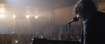 Movie still from “Frank” (2014), directed by Lenny Abrahamson – A microphone in front of a microphone stand in front of an audience; Medium shot, Low angle