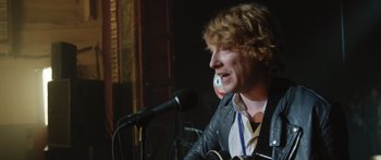 Movie still from “Frank” (2014), directed by Lenny Abrahamson – A man is singing into a microphone while holding a guitar; Close Up shot, Over the shoulder angle