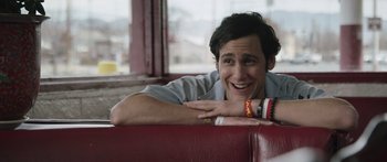 Movie still from “Frank” (2014), directed by Lenny Abrahamson – A man smiling while sitting on a red couch; Close Up shot, Over the shoulder angle