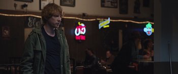 Movie still from “Frank” (2014), directed by Lenny Abrahamson – A man standing in front of a neon sign in a restaurant; Medium shot, Over the shoulder angle