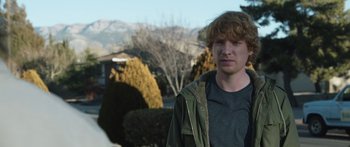 Movie still from “Frank” (2014), directed by Lenny Abrahamson – A young man standing in front of some bushes; Close Up shot, Over the shoulder angle