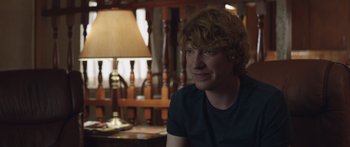 Movie still from “Frank” (2014), directed by Lenny Abrahamson – A young man sitting at a table in front of a lamp; Close Up shot, Over the shoulder angle