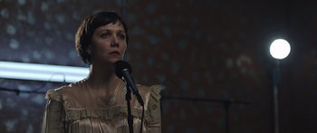 Movie still from “Frank” (2014), directed by Lenny Abrahamson – A woman standing in front of a microphone in a room; Close Up shot, Over the shoulder angle