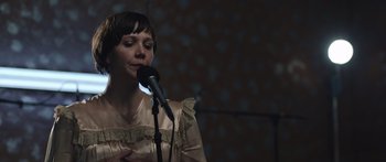 Movie still from “Frank” (2014), directed by Lenny Abrahamson – A woman is holding a microphone in her hands; Close Up shot, Low angle
