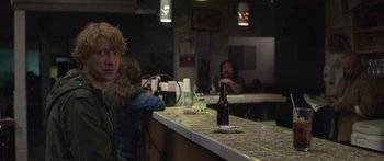 Movie still from “Frank” (2014), directed by Lenny Abrahamson – A man sitting at a counter with a bottle of beer on the counter; Medium shot, Over the shoulder angle