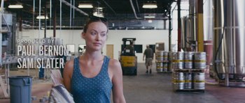 Movie still from “Drinking Buddies” (2013), directed by Joe Swanberg – A woman standing in a warehouse next to a forklift; Close Up shot, Over the shoulder angle