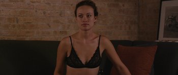 Movie still from “Drinking Buddies” (2013), directed by Joe Swanberg – A woman in a black bra sitting in front of a brick wall; Medium shot, High angle