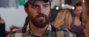Movie still from “Drinking Buddies” (2013), directed by Joe Swanberg – A person with a beard wearing a hat; Close Up shot, Over the shoulder angle