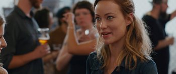 Movie still from “Drinking Buddies” (2013), directed by Joe Swanberg – A woman's face in front of a group of people; Close Up shot, Over the shoulder angle