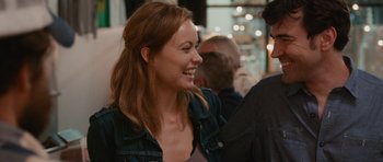 Movie still from “Drinking Buddies” (2013), directed by Joe Swanberg – A woman smiles while standing next to a man; Close Up shot, Over the shoulder angle