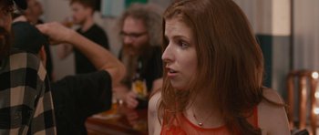 Movie still from “Drinking Buddies” (2013), directed by Joe Swanberg – A woman sitting at a table in front of other people; Close Up shot, Over the shoulder angle
