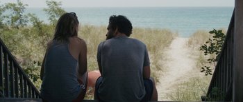 Movie still from “Drinking Buddies” (2013), directed by Joe Swanberg – A man and a woman sitting next to each other on the beach; Medium shot, Over the shoulder angle