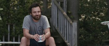 Movie still from “Drinking Buddies” (2013), directed by Joe Swanberg – A man sitting on the ground holding a cup; Medium shot, Over the shoulder angle