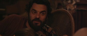Movie still from “Drinking Buddies” (2013), directed by Joe Swanberg – A bearded man sitting in a wicker chair looking at the camera; Close Up shot, Over the shoulder angle