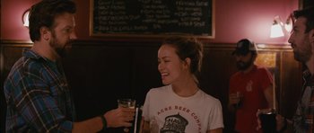 Movie still from “Drinking Buddies” (2013), directed by Joe Swanberg – A woman holding a glass of beer in her right hand; Medium shot, Over the shoulder angle