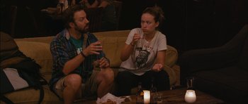 Movie still from “Drinking Buddies” (2013), directed by Joe Swanberg – A man and a woman sitting on a couch drinking beer; Medium shot, Over the shoulder angle