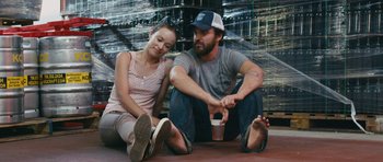 Movie still from “Drinking Buddies” (2013), directed by Joe Swanberg – A man and a woman sitting next to each other on the ground; Medium shot, High angle